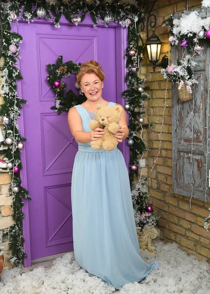 Pelüş ayılı, uzun boylu, çekici bir kadın. Mutlu bir kadın oyuncak ayı gösteriyor. Güzel süslenmiş evinin kapısında dikilirken.