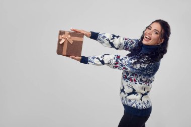 Güzel bir kadın beyaz bir arka planda, Noel süveteri içinde bir hediye kutusu tutuyor..