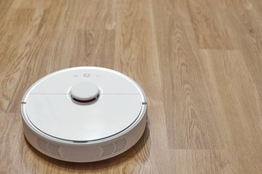 Temizlik bittikten sonra lamine yaprakların üzerinde beyaz bir robot elektrikli süpürge. Odaya robot bir elektrikli süpürge giriyor..