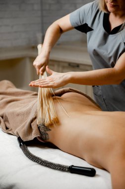 Bir kadın, masaj masasında genç bir kıza bambu süpürge masajı yapıyor. Bambu süpürgeleri..