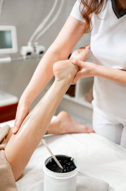 Kıza anti-selülit ayak masajı ve siyah önlük kremi veriliyor. Güzellik salonunda bacak deplasmanı. Masaja yakın çekim. Depilasyon yakın plan.