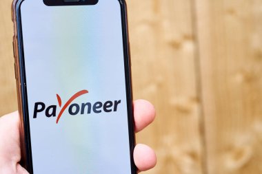 Ukraine, Kyiv, May 3, 2022 - Hand holding smartphone with payoneer logo on wooden background