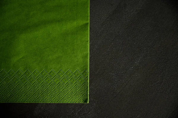 A beautiful green napkin lies on a black texture table with a corner to the side. Space for labels — Stock fotografie