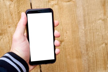 A mans hand holds a mobile phone against a background of wood texture. Phone template with white screen