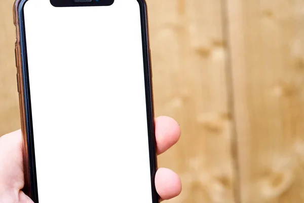 Une main d'homme tient un téléphone portable sur un fond de texture de bois. Modèle de téléphone avec écran blanc — Photo
