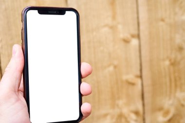 Bir adamın eli ahşap dokunun arka planına karşı cep telefonu tutar. Beyaz ekranlı telefon şablonu