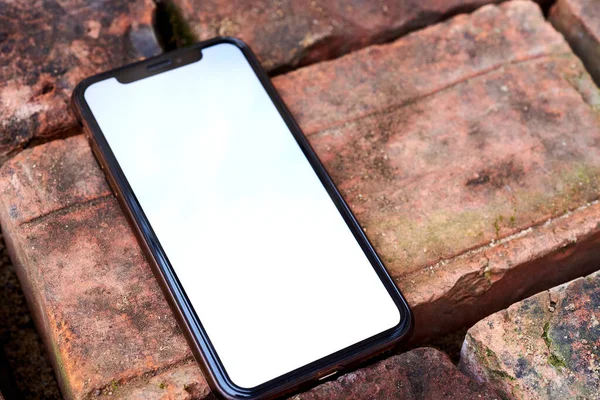 Sjabloon voor mobiele telefoon met wit scherm. De smartphone ligt op de textuur van de baksteen. Mockup van een mobiele telefoon — Stockfoto