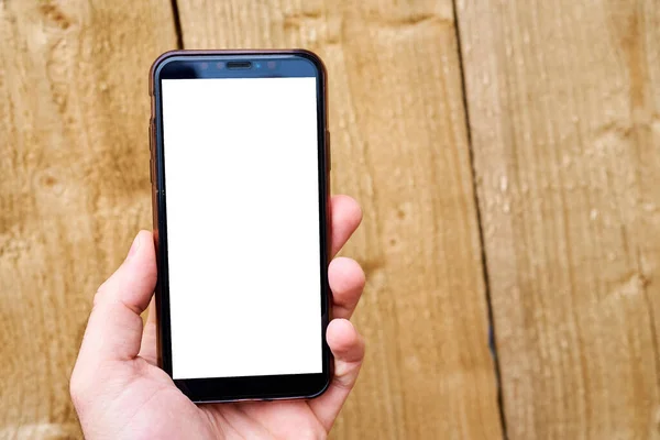 A mans hand holds a mobile phone against a background of wood texture. Phone template with white screen — Stockfoto