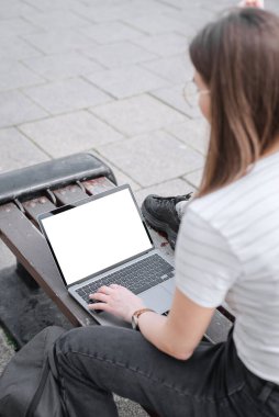 Kızlar bir bankta oturan dizüstü bilgisayarda el yazısı yazıları yazıyorlar. Sokakta boş beyaz ekranlı bir dizüstü bilgisayar modeli. Ürününüzü dizüstü bilgisayarınıza tanıtın.
