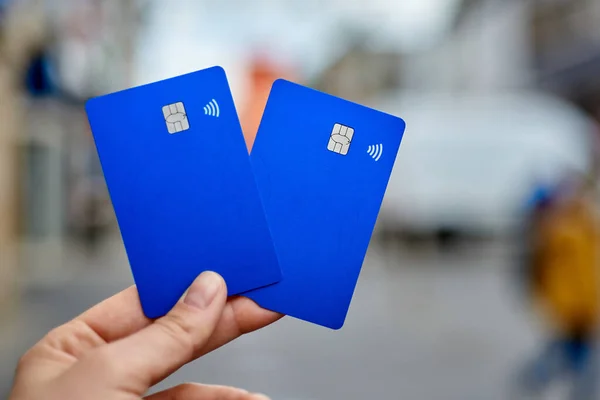 Bank cards are close-up against the background of a blurred street. Chip and contactless payment in the bank card. Blue modern bank card.