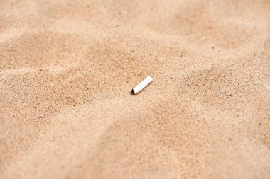 A white cigarette butt lies on beautiful yellow sand. Pollution of beaches. Combating smoking in public places. Nicotine addiction. Dirty sand. Bad habits. A cigarette in the sand.