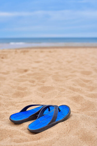 Mens rubber flip-flops stand on beautiful yellow sand. The concept of recreation in hot countries. Womens flip-flops against the backdrop of the blue sea and sand. relax on the beach.