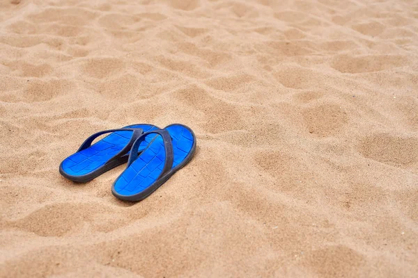 Bright blue mens rubber slates stand on the beautiful yellow sea sand. The concept of recreation in hot countries. Beach holidays. Clean sand.