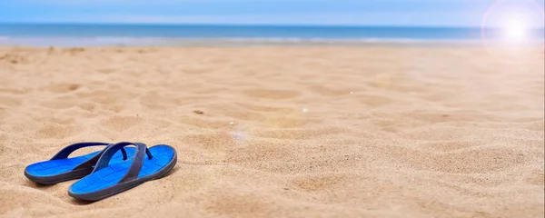 Mens rubber flip-flops stand on beautiful yellow sand. The concept of recreation in hot countries. Womens flip-flops against the backdrop of the blue sea and sand. relax on the beach. Banner.