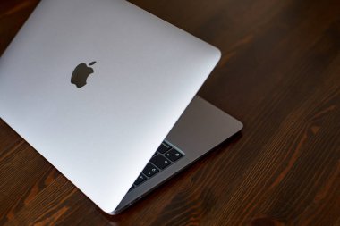 UK, Newcastle upon Tyne, 20 July 2022 - MacBook Air 2020-2022. An ajar MacBook Air stands on a wooden table. The image of the Apple logo on the lid and a view of the glowing keyboard. Side view.