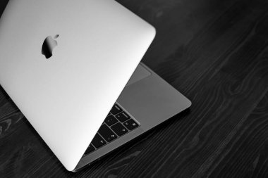 UK, Newcastle upon Tyne, 20 July 2022 - MacBook Air 2020-2022. An ajar MacBook Air stands on a wooden table. The image of the Apple logo on the lid and a view of the glowing keyboard. Side view. BW