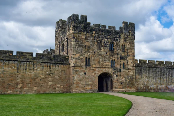 Alnwick Castle. The walls of an ancient castle in the north of England. The old castle and its gate against the blue sky and green lawn.