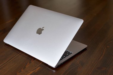 UK, Newcastle upon Tyne, 20 July 2022 - MacBook Air 2020-2022. An ajar MacBook Air stands on a wooden table. The image of the Apple logo on the lid and a view of the glowing keyboard. Side view.