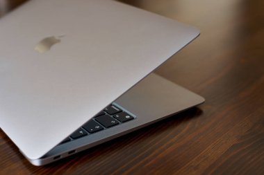 UK, Newcastle upon Tyne, 20 July 2022 - MacBook Air 2020-2022. An ajar MacBook Air stands on a wooden table. The image of the Apple logo on the lid and a view of the glowing keyboard. Side view.