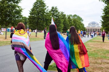 Newcastle Gururu. Genç insanların omuzlarında LGBTQ bayrakları var. Azınlık bayrakları omuzlarında üç genç kız geçit töreninde yürüyor..