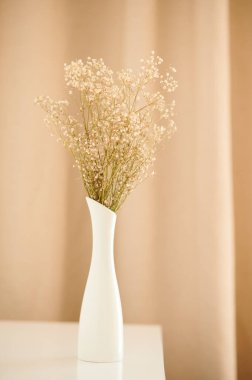 Dried flowers in a white vase stand on a golden background. Minimalistic Scandinavian interior.