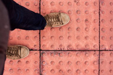 Tactile tiles for the blind. Panels for the blind laid on asphalt. Guide tape for the disabled. Red new tactile tiles for the visually impaired. A man walks on special tactile tiles on the road.