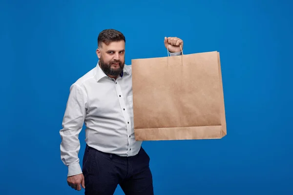 A Caucasian-looking man holds a large brown paper bag. A man in a white shirt with shopping bags on a blue background. Space for text on the shopping banner ad. Banner for discounts.