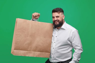 A Caucasian-looking man holds a large brown paper bag. A man in a white shirt with shopping bags on a green background. Space for text on the shopping banner ad. Banner for discounts.