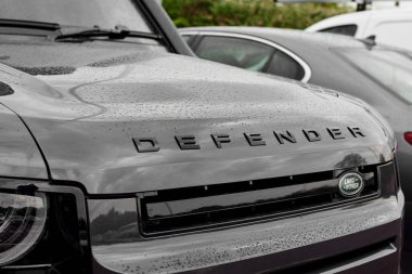 UK, Newcastle, 27 August 2022: 2022 Land Rover Defender in black is parked in the parking lot. Total black car. Chandelier on the SUV. Beam of light. Close-up of the DEFENDER logo.