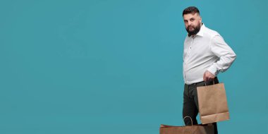 A Caucasian-looking man with a brown paper bag on a blue background. A man with a white shirt with shopping bags. Studio shot of a man with purchases. Space for text.