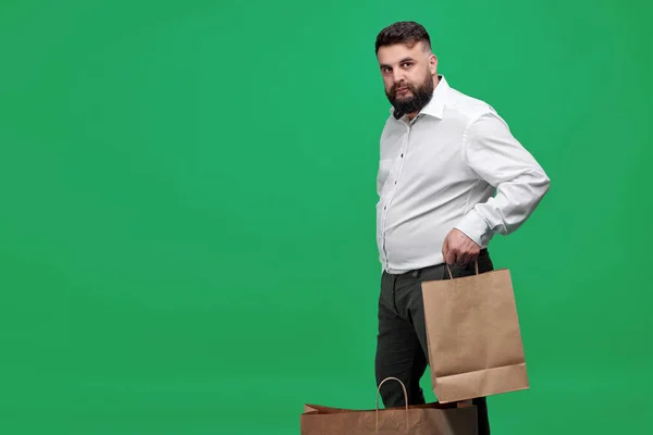 A Caucasian-looking man with a brown paper bag on a green background. A man with a white shirt with shopping bags. Studio shot of a man with purchases.
