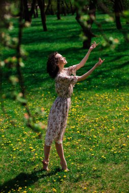 Bahar çiçekli bahçede poz veren kıvırcık saçlı çekici bir kadın.