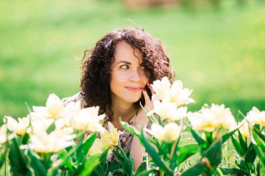 Bahar çiçekli bahçede poz veren kıvırcık saçlı çekici bir kadın.