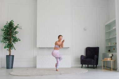 Sağlık konsepti. Genç ve güzel bir kadın modern bir odada yoga egzersizi yapıyor.