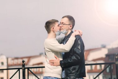 Tıbbi maske takan, şehirde sarılıp öpüşen genç eşcinsel çift..