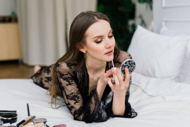 Güzel bayan makyaj yapıyor ve yatak odasında saç yapıyor. Oldukça uzun saçlı çekici bir genç bayan.