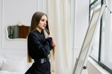 Güzel bayan makyaj yapıyor ve yatak odasında saç yapıyor. Oldukça uzun saçlı çekici bir genç bayan.