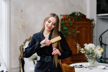 Güzel bayan makyaj yapıyor ve yatak odasında saç yapıyor. Oldukça uzun saçlı çekici bir genç bayan.