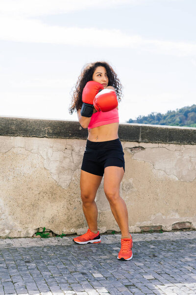 Photo of strong fitness woman boxer in gloves posing outdoors.
