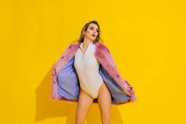 Lüks kürk manto ve vücut giysisiyle poz veren muhteşem genç bir kadın. Moda, güzellik. Stüdyo çekimi.