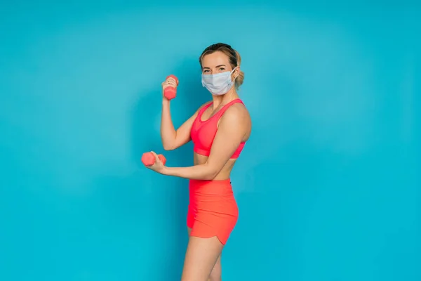 Woman in a face protection mask and fitness wear isolated over blue background.