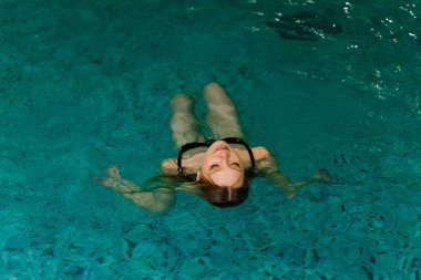 Yüzme havuzunda dinlenen, mayo giymiş güzel bir kadının portresi..