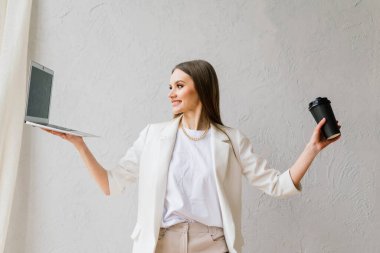 Oturma odasında oturmuş kahve içerken dizüstü bilgisayarda çalışan güzel genç bir kadın.