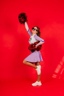 Stüdyoda poz veren genç bayan ponpon kız, kırmızı ve mavi üzerine izole edilmiş.