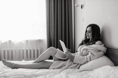 Evin içinde, büyük pencerelerin yanında beyaz bir bornozla poz veren güzel, harika bir genç kadın resmi..