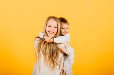 Happy brother and sister studio portrait on a yellow background