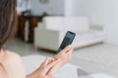 Masada oturan genç bir kız öğrenci, çalışırken akıllı telefon kullanıyor..