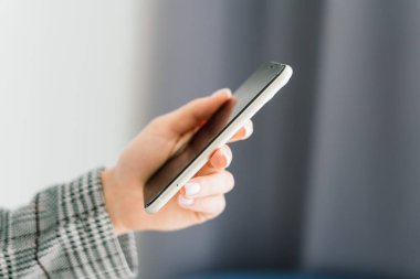 Masada oturan genç bir kız öğrenci, çalışırken akıllı telefon kullanıyor..