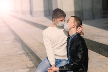 Tıbbi maske takan genç eşcinsel çift şehirde sarılıyor..