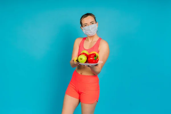Woman in a face protection mask and fitness wear isolated over blue background.